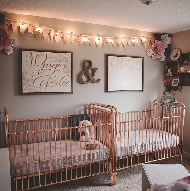 a cute and glam twin nursery with grey walls, rose gold cribs, a bunting and lights, pretty artworks and paper flowers