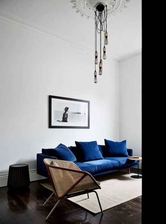 a dreamy living room done in contrasting colors, with a navy sofa, cane chairs, round side tables and bulbs hanging from the ceiling medallion