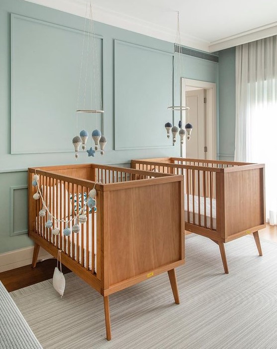 a dreamy twin nursery with blue paneled walls, lovely stained cribs, mobiles and neutral textiles is a very welcoming space