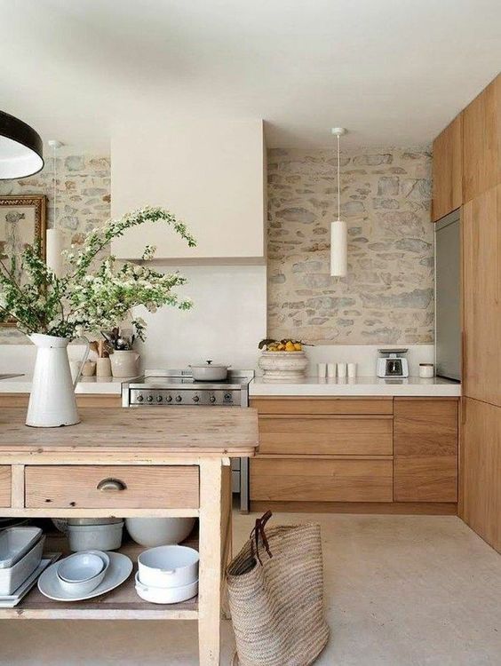 a fantastic modern rustic kitchen with light-stained cabinets, white stone countertops, a table kitchen island and a stone accent wall