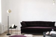 a fantastic neutral living room with a deep purple velvet sofa and a matching ottoman, neutral textiles, a round coffee table and a floor lamp