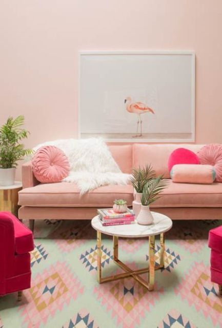 a glam living room with a pink sofa and pillows, hot pink chairs, a marble coffee table, a bright printed rug and potted greenery