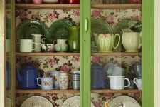 a green glass cabinet with colorful floral wallpaper inside for a chic and bold look, it can be used in any vintage kitchen or dining space