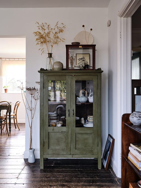 a green shabby chic cabinet with glass doors is used for storing tableware and porcelain in a rustic dining room or kitchen