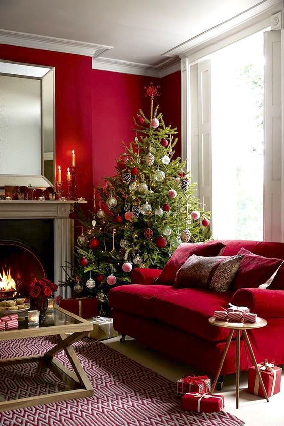 a hot red living room with a fireplace, a depe red sofa, a glass coffee table, a Christmas tree with red and white ornaments and candles