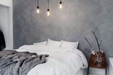 a laconic Scandinavian bedroom with a grey limewashed wall, a white bed with white bedding, a vase on a stand, a bulb chandelier