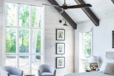 a large airy farmhouse bedroom done with white walls, dark stained ceiling beams and comfy furniture