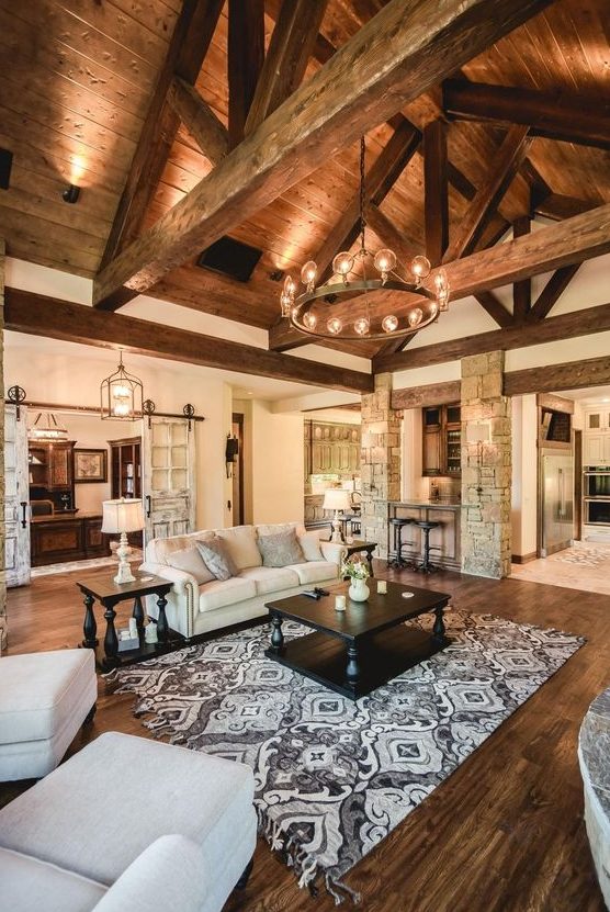 a large rustic living room with an attic ceiling and beams, stone clad pillars and a stained wooden floor