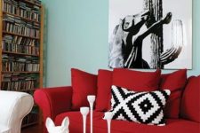 a light blue living room with an open storage unit, a bold red sofa that contrasts the walls, a coffee table and a graphic artwork