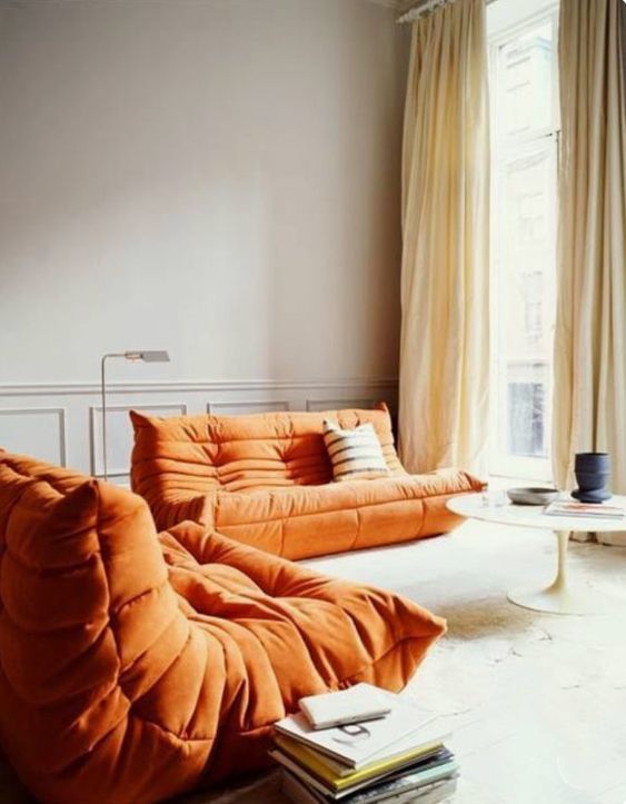 a light filled living room with low orange loveseats, a round table and a neutral textural rug   who needs more than that to invite friends for a coffee