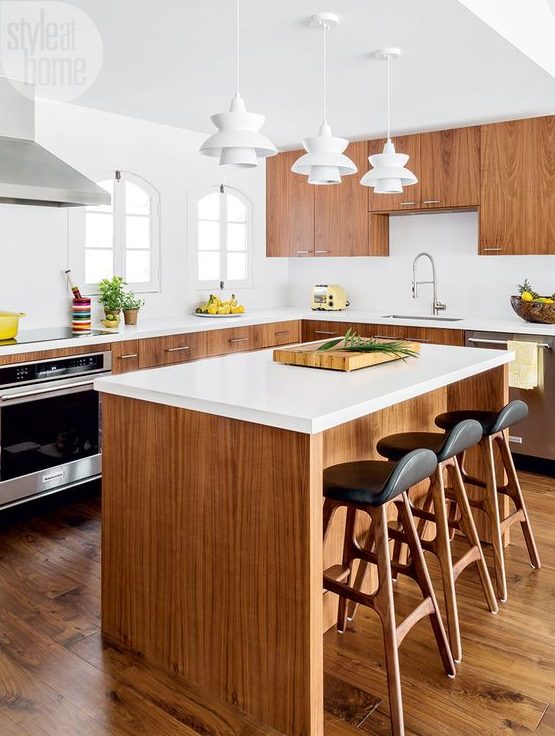 a light filled mid century modern kitchen with rich stained cabinets, white countertops, white sculptural pendant lamps