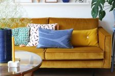 a lively living room with a mustard sofa, a round table, a ledge gallery wall and touches of blue for a contrast
