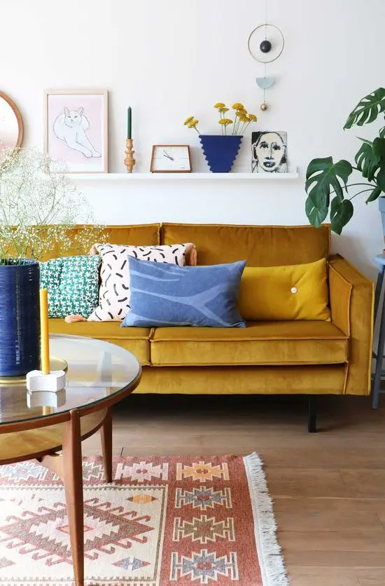 a lively living room with a mustard sofa, a round table, a ledge gallery wall and touches of blue for a contrast