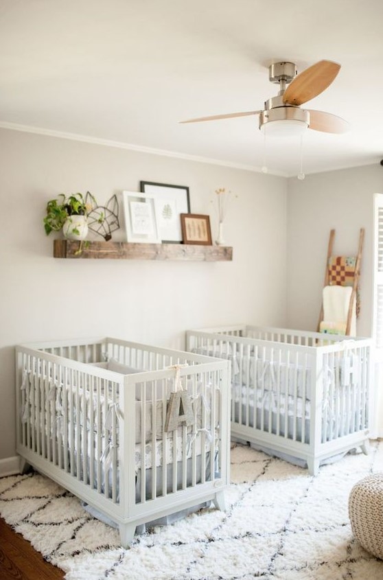 a lovely farmhouse twin nursery with grey walls, white cribs, a stained shelf with artworks and potted greenery plus a ladder