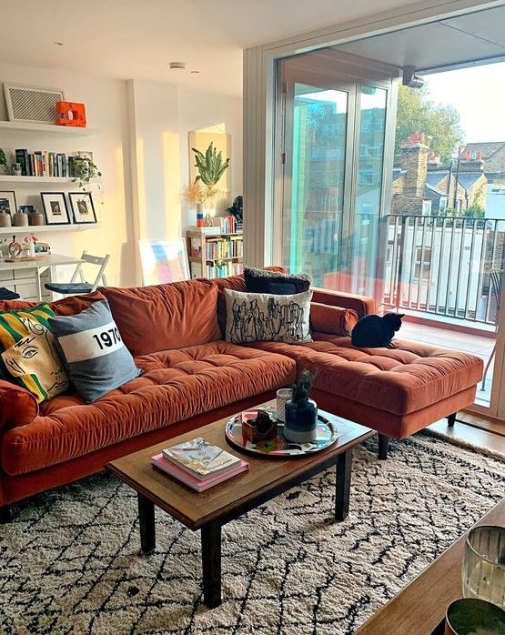 a lovely living room with a rust colored sectional, a low table, floating shelves and potted plants here and there
