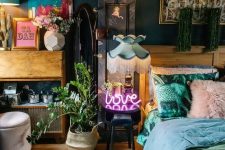 a lovely maximalist bedroom with dark walls and a ceiling, with mid-century modern furniture, pastel bedding, a potted plant, a neon light and colorful artworks