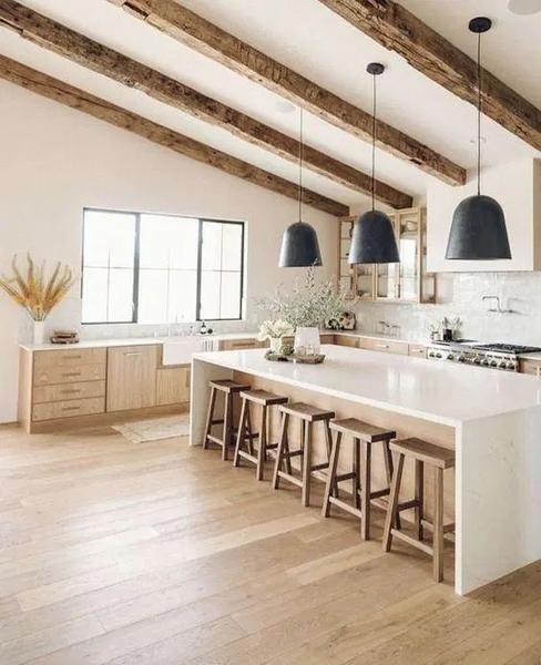 a lovely modern rustic kitchen with light-stained cabinets, white stone countertops, wooden beams, black pendant lamps and a white tile backsplash