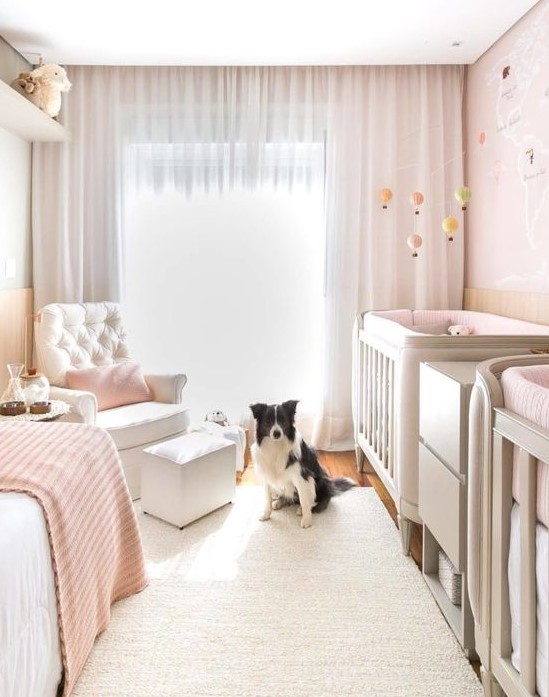 a lovely twin nursery with blush walls, grey cribs, a creamy chair with a footrest and a daybed, blush textiles and pretty mobiles