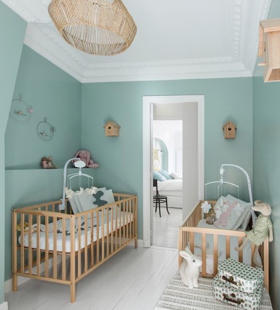 a lovely twin nursery with green walls, matching stained cribs, matching mobiles and a rattan pendant lamp