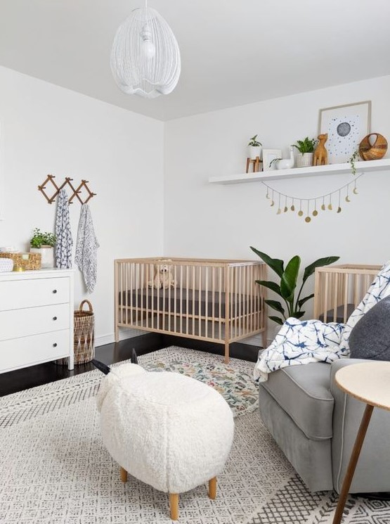 a lovely neutral nursery with stained cribs, a grey chair, an animal-shaped ottoman, a white dresser, a shelf with artworks