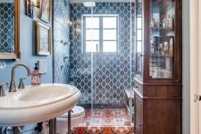 a maximalist bathroom with blue walls and blue tiles, a red mosaic tile floor, a stained storage cabinet and a smal gallery wall