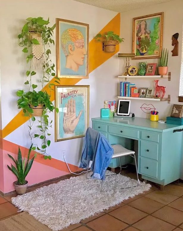 a maximalist home office with a color block accent wall, a turquoise desk, floating shelves, colorful art and lots of potted plants
