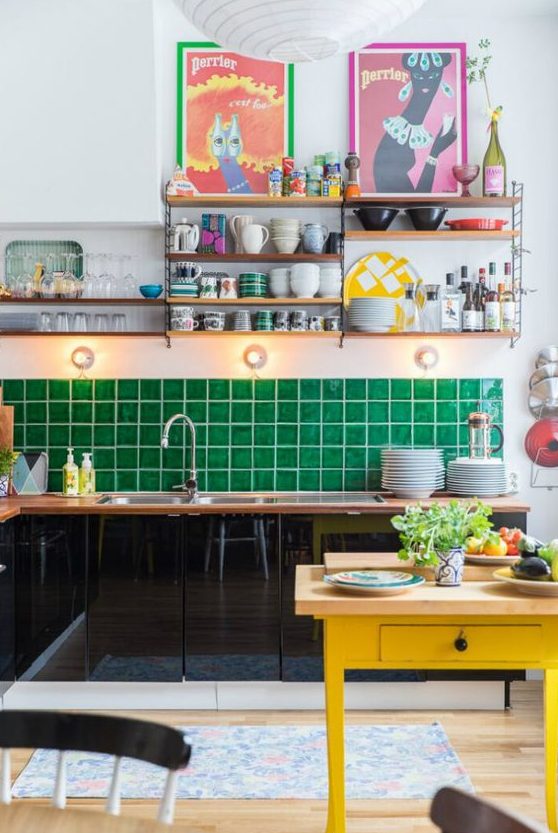 a maximalist kitchen with black sleek cabinets, an emerald tile backsplash, a yellow table, colorful artworks and open shelves