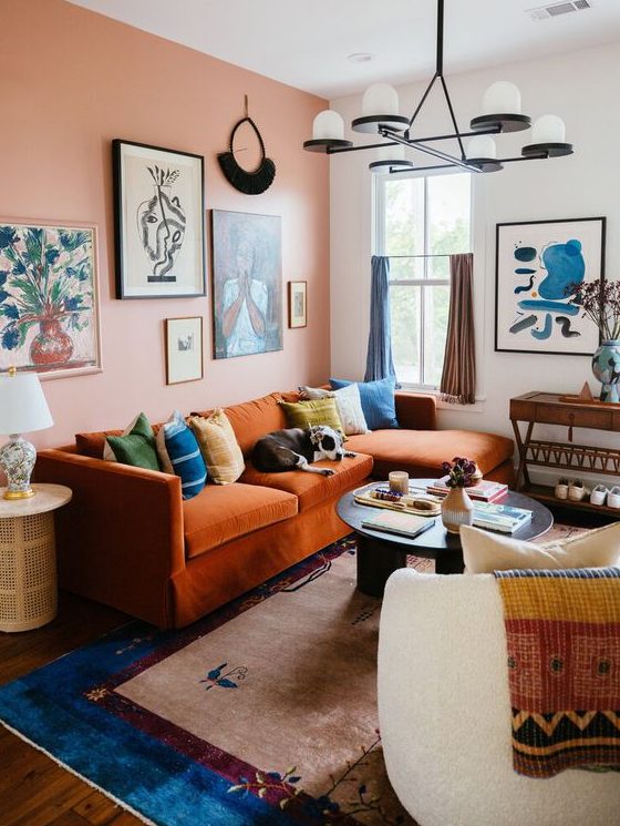 a maximalist living room with a pink accent wall, an orange sofa with colorful pillows, neutral furniture and bold textiles plus colorful curtains