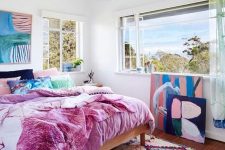 a maximalist ocean bedroom with simple furniture, colorful bedding and a bold artwork plus a gorgeous view