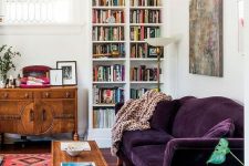 a mid-century modern living room done in neutrals and filled with color – a printed rug, a deep purple sofa, stained furniture and a built-in bookcase