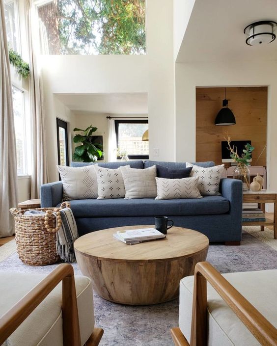 a mid-century modern living room with a blue sofa, neutral pillows, a round wooden table, neutral chairs, a basket with blankets