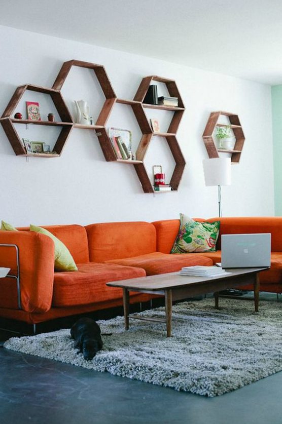 a mid century modern living room with an orange sofa, hexagon shelves, a low table and colorful pillows is welcoming