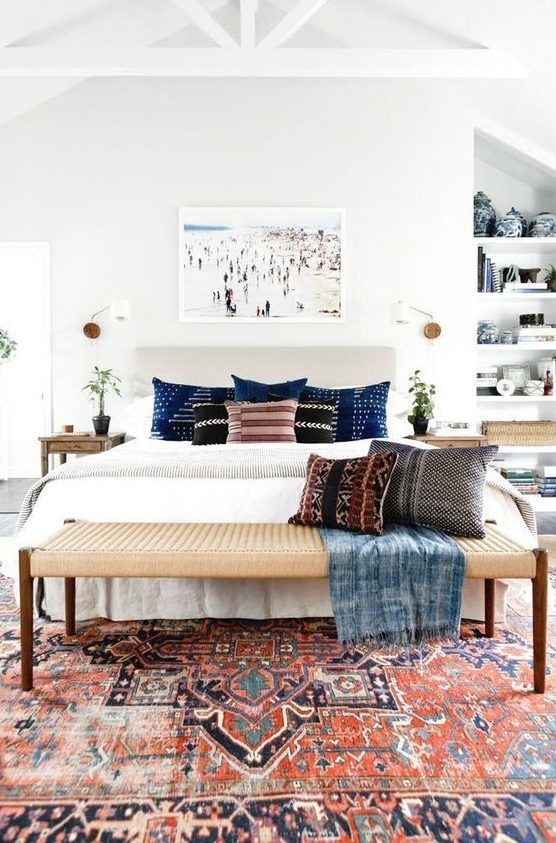 a mid century modern meets boho bedroom with a boho rug, a woven bench, a built in shelving unit and an artwork