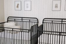 a mid-century modern nursery with an accent wallpaper wall, black metal cribs, a geometric lamp and layered rugs