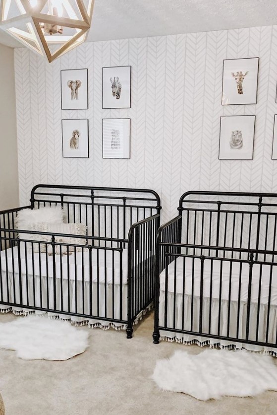 a mid-century modern nursery with an accent wallpaper wall, black metal cribs, a geometric lamp and layered rugs