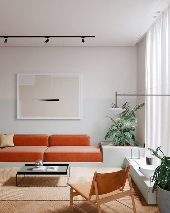 a minimalist living room with an orange velvet sofa, a low table and a leather chair plus potted plants and an abstract artwork
