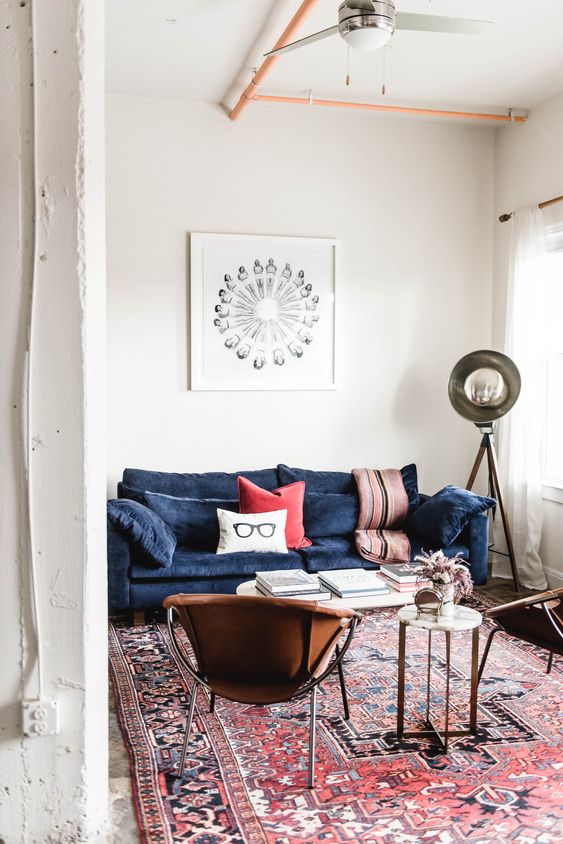 a modern boho living room with a navy sofa, a couple of leather chairs, a coffee table and a side table, some lamps