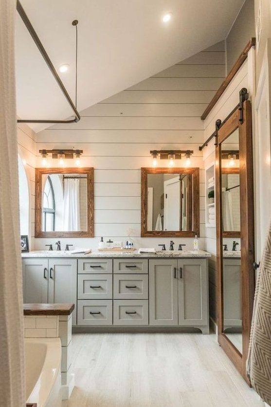 a modern farmhouse bathroom with light-colored vanities, wooden frame mirrors and whitewashed floors and walls
