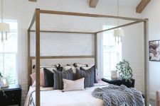 a modern farmhouse bedroom with a faux white brick wall, a frame bed with neutral bedding, a white bench and wodoen beams on the ceiling