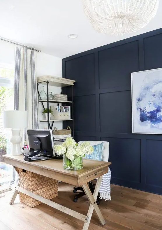 a modern farmhouse home office with a navy statement wall, a wooden trestle desk, a white chair and a basket