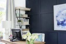 a modern farmhouse home office with a navy statement wall, a wooden trestle desk, a white chair and a basket