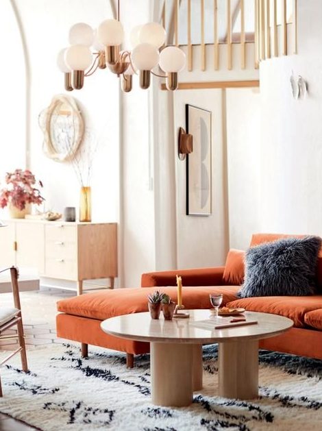 a modern living room done in neutrals, with a rust-colored sectional, a low round table and a mid-century modern chandelier to light up the space