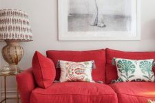 a modern living room with a bold red sofa, printed pillows, a statement artwork, a printed lamp and stacks of books