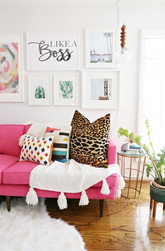 a modern living room with a hot pink sofa, printed pillows, a chic gallery wall, a pendant bulb and potted plants