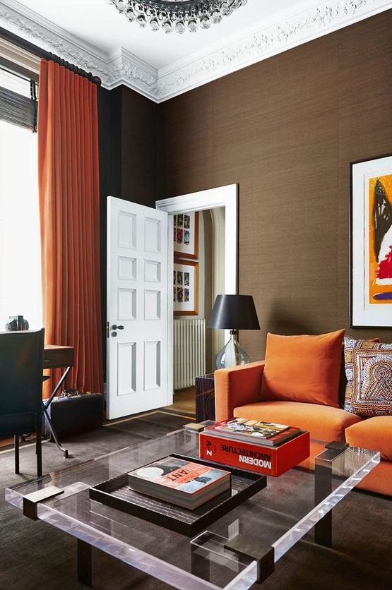 a modern living room with an orange sofa, a low acrylic table, a desk and a leather chair plus a crystal chandelier
