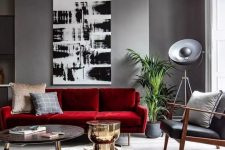 a modern living room with grey walls, a bold red sofa, a black leather chair, a monochromatic artwork and a round table
