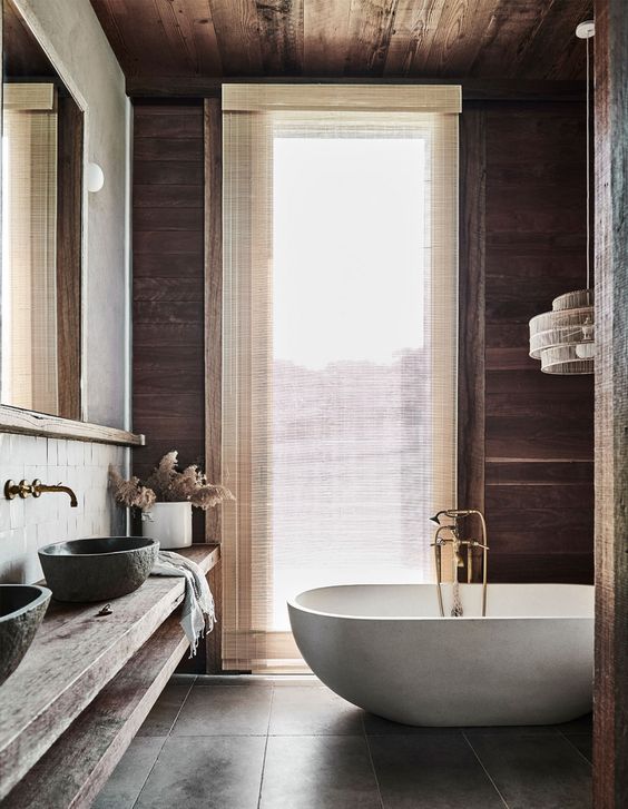 a modern rustic bathroom with a wooden vanity composed of two shelves, an oval tub, walls and the ceiling clad with wood and a large window