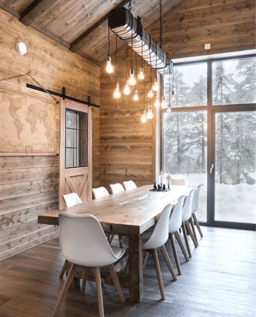a modern rustic dining room with the ceiling, walls and a floor clad with wood, a wooden dining table, white Eames chairs and a bulb chandelier