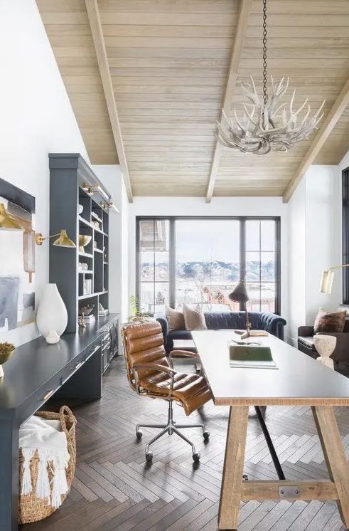 a modern rustic home office with a large graphite grey storage unit, a wooden desk, a leather chair and an antler chandelier