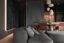 a moody and elegant slate grey space, with a low sofa and daybed, with lit up artworks, pendant lamps and copper furniture